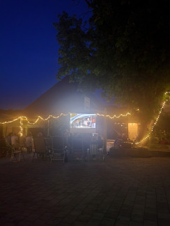 Mit Lichterketten erleuchteter Innenhof des Jugendhilfezentrums in Schnaittach vor Abendhimmel, in der Mitte die Leinwand, davor Zuschauende auf mitgebrachten Stühlen